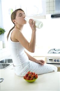 Mujer, sentada en la mesa de la cocina, con fresones y bebiendo leche de la botella.