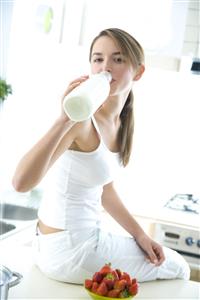 Mujer, sentada en la mesa de la cocina, con fresones y bebiendo leche de la botella.