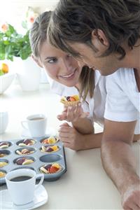 Pareja, en la cocina, comiendo tartaletas de frutas.