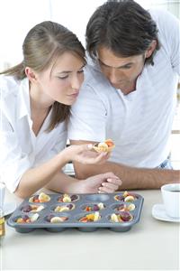 Pareja, en la cocina, comiendo tartaletas de frutas.