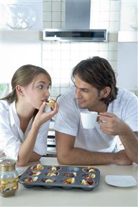 Pareja, en la cocina, comiendo tartaletas de frutas y mirandose a los ojos.