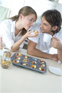 Pareja, en la cocina, comiendo tartaletas de frutas y mirandose a los ojos.