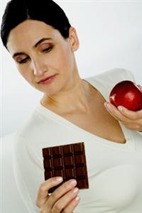 Mujer dudando entre comerse una manzana o chocolate. Alta resolución disponible. Contactar con: firofoto@firofoto.com Telf.: 93 211 25 93