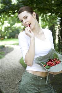 Jardineria. Mujer cogiendo una cereza de un sombrero lleno de cerezas recien cogidas. 