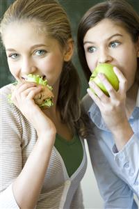 Dos chicas adolescentes comiendo. Una, un bocadillo vegetal y la otra, una manzana. Primer plano.