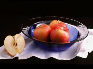 Frutero con tres manzanas y otra cortada.