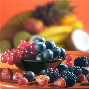 Plato con frutas del bosque: moras,fresitas,grosella y arandanos, detras fruta tropical desenfocada.