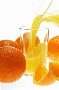 Pouring orange juice into glass among oranges