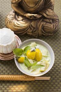 Coconut soup with fish and Thai aubergines in front of Buddha