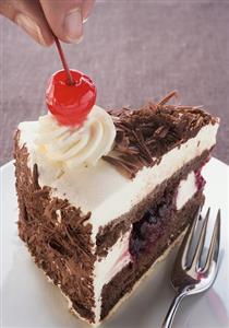 Decorating a piece of Black Forest gateau with cherry