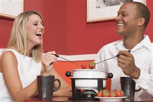 Young woman & man eating chocolate fondue with strawberries