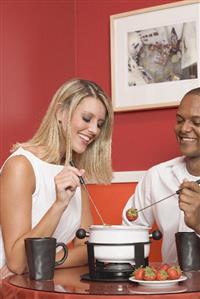 Young woman & man eating chocolate fondue with strawberries