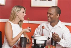 Young woman & man eating chocolate fondue with strawberries