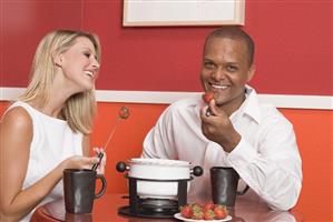 Young woman & man eating chocolate fondue with strawberries