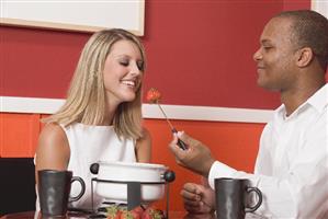 Young woman & man eating chocolate fondue with strawberries