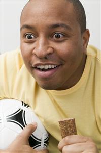 Young man with football and chocolate bar watching TV