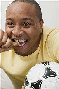 Young man with football and chocolate bar watching TV