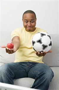 Young man with apple and football watching TV