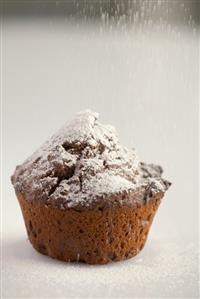 Sprinkling a chocolate muffin with icing sugar