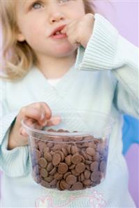 Small girl eating chocolate buttons out of plastic tub