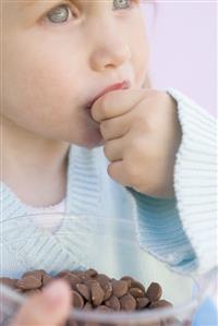 Small girl eating chocolate buttons out of plastic tub