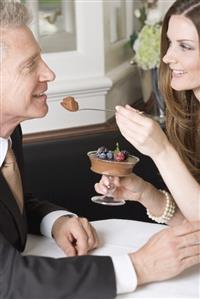 Woman offering man spoonful of chocolate cream in restaurant