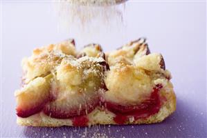 Sprinkling piece of plum cake with sugar