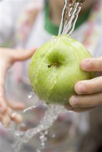 Child holding green apple under running water