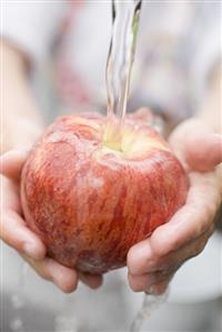 Child's hands holding red apple under running water