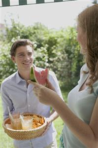 Man holding basket of drinks & chips, woman with watermelon