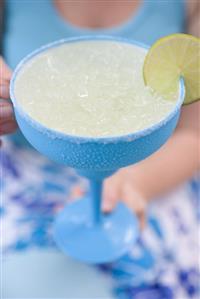 Woman holding a lime cocktail in a turquoise glass