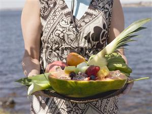 Woman holding tray of fresh exotic fruit by sea