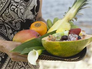 Woman holding tray of fresh exotic fruit by sea