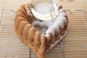 Sprinkling heart-shaped ring cake with icing sugar