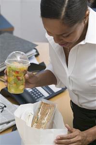 Woman with packed lunch (sandwich, fruit salad) in the office