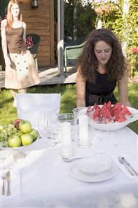 Woman carrying pieces of watermelon to table laid in garden