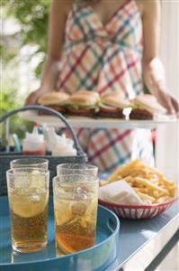 Iced tea and chips on table, woman serving hamburgers