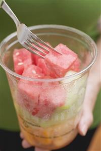 Woman holding plastic tub of diced melon and watermelon.