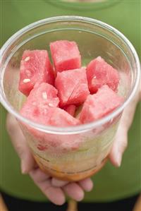 Woman holding plastic tub of diced melon and watermelon.