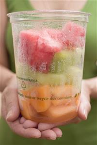 Woman holding plastic tub of diced melon and watermelon.