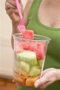 Woman eating diced melon and watermelon out of plastic tub