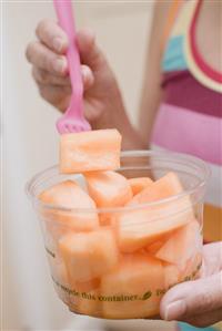 Woman eating diced melon out of plastic tub