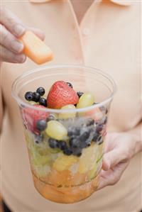 Woman taking piece of melon out of plastic tub of fruit salad