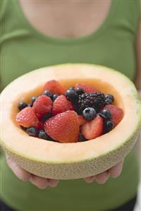 Woman holding fresh berries in hollowed-out cantaloupe melon