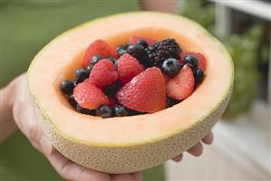 Woman holding fresh berries in hollowed-out cantaloupe melon