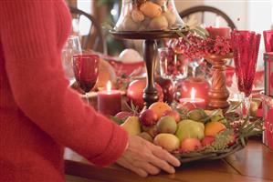 Woman placing bowl of fruit on table laid for Christmas