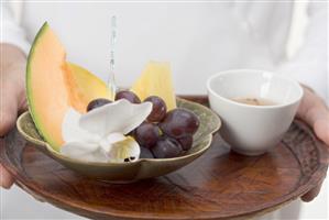 Woman holding dish of fruit and tea bowl on tray