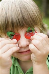 Small boy holding cherry jelly sweets in front of his eyes