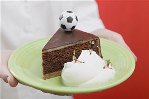 Person holding piece of Sacher torte with cream & football