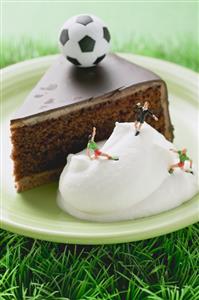 Piece of Sacher torte with cream and toy football